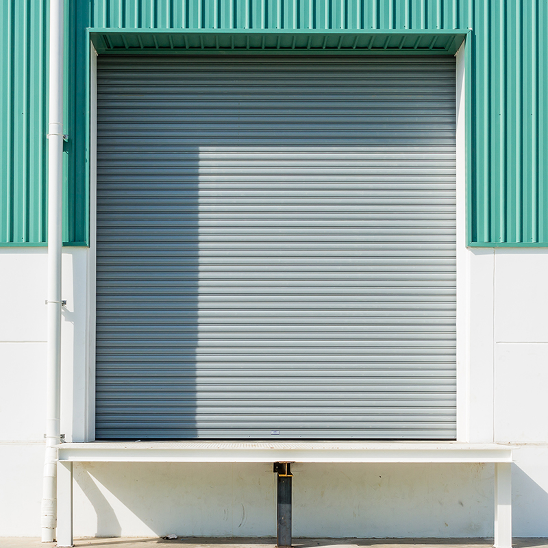 Roller shutter door and dock leveler ramp outside factory building for industrial background.